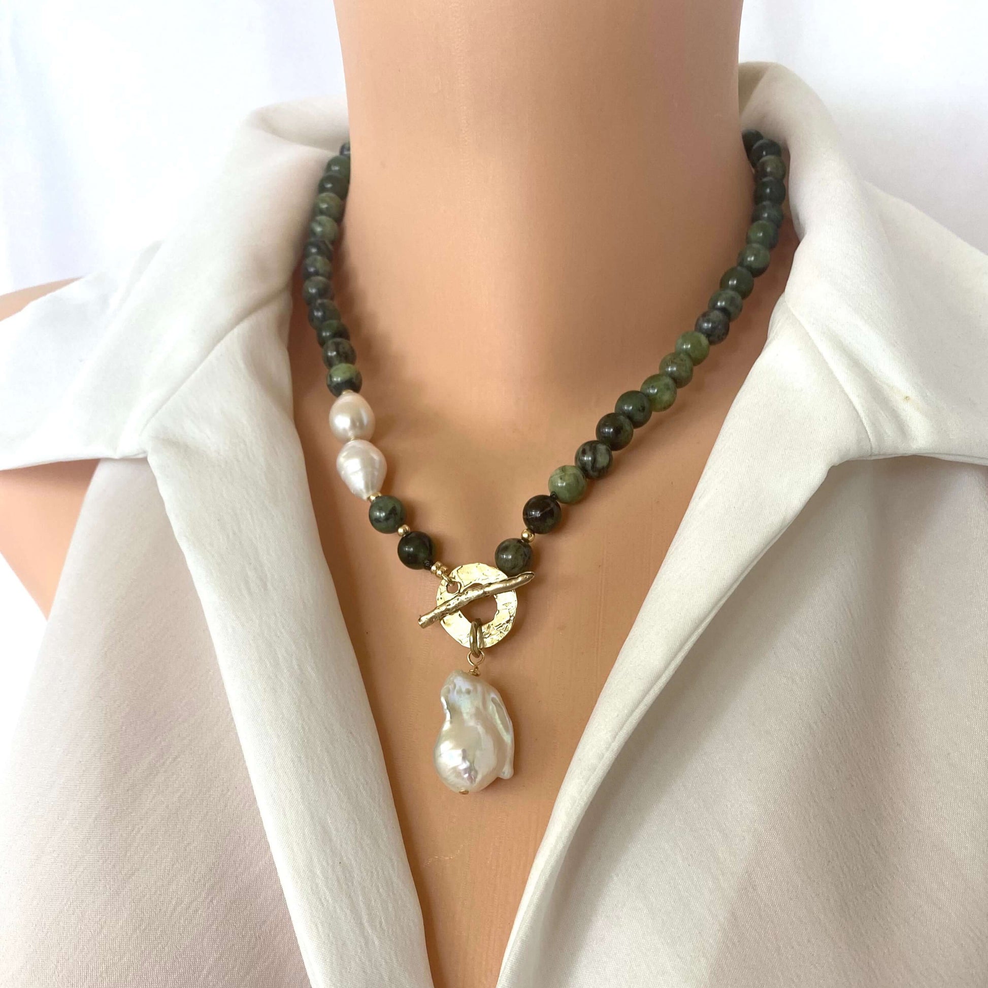 Necklace with green beads and a large pearl pendant on a mannequin wearing a white shirt.