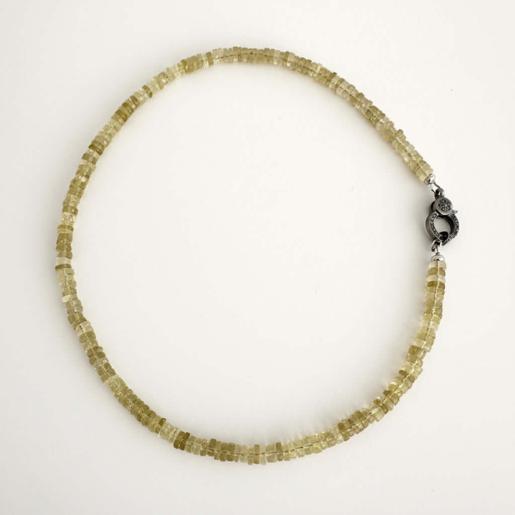 A beaded necklace made of small, faceted translucent yellow-green crystal beads, featuring a dark metal lobster clasp, displayed on a plain white background.