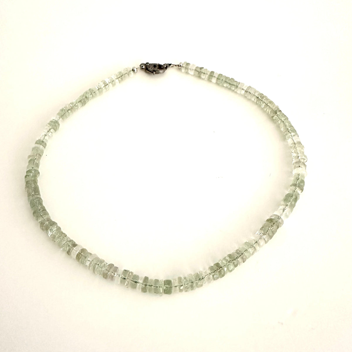A beaded necklace made of small, faceted light green gemstone beads, arranged in a circle on a plain white background.