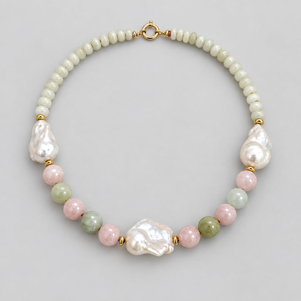 A handmade beaded necklace featuring a strand of small cream-colored beads, irregular white baroque pearls, polished pink and green beads, and gold spacer rings, displayed on a neutral light beige background.
