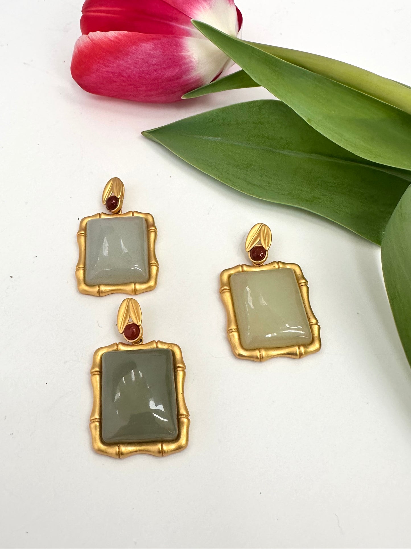 Gold-framed pendants with green stones and red gemstones on a white background with tulip leaves.