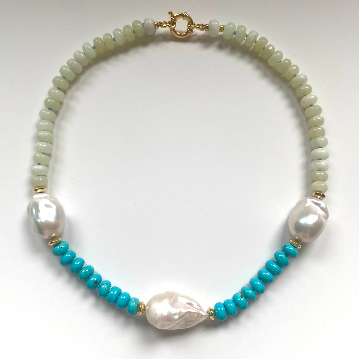A beaded necklace featuring light green beads, white baroque pearls, and bright turquoise blue beads separated by small gold spacer beads, displayed on a clean white background.