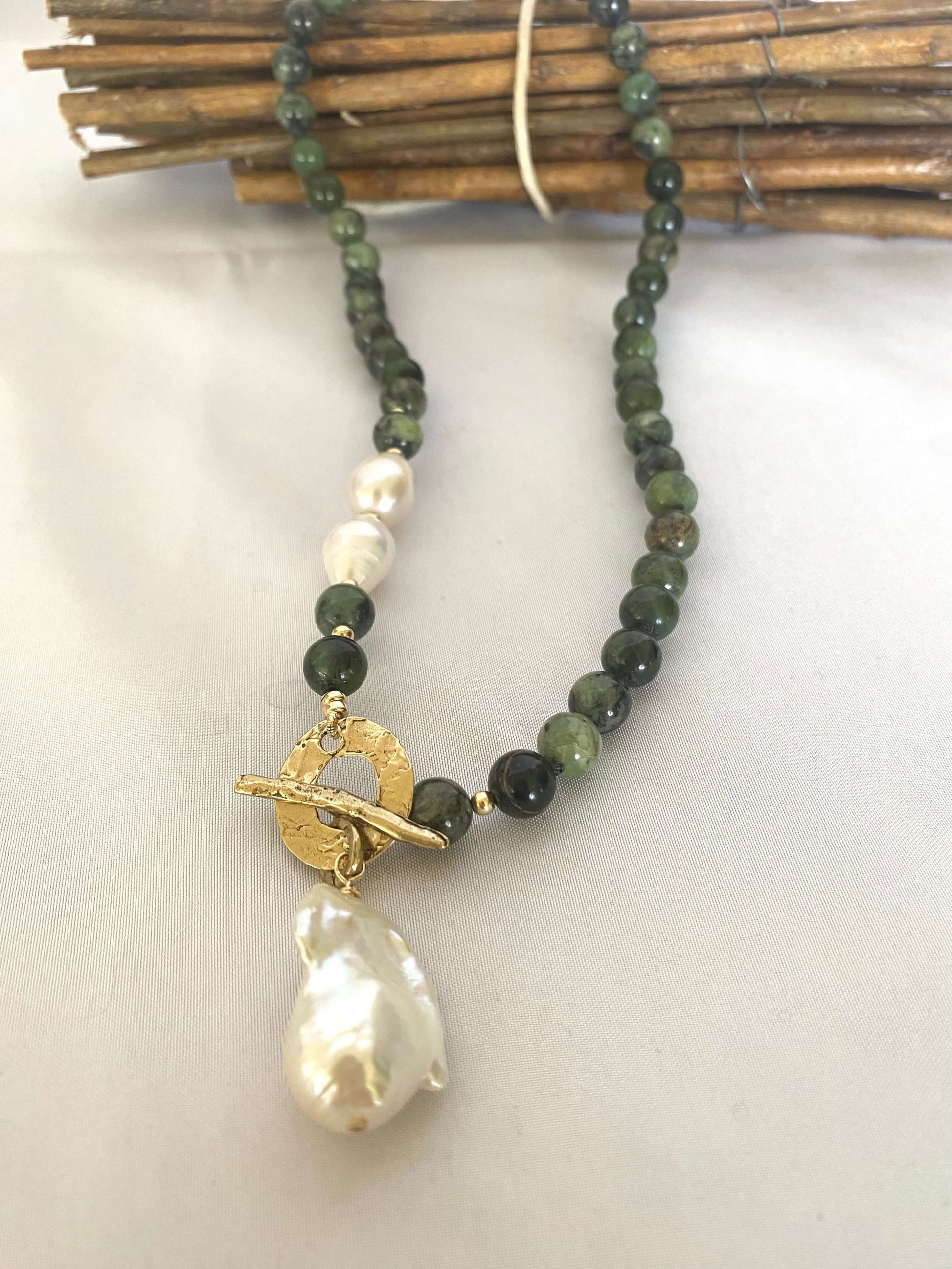 Necklace with green beads and a large pearl pendant on a white background