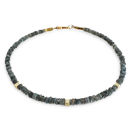 A raw stone disc necklace featuring dark gray and blue-gray lapis lazulii with small gold spacer beads and a gold lobster clasp, shown on a plain white background.