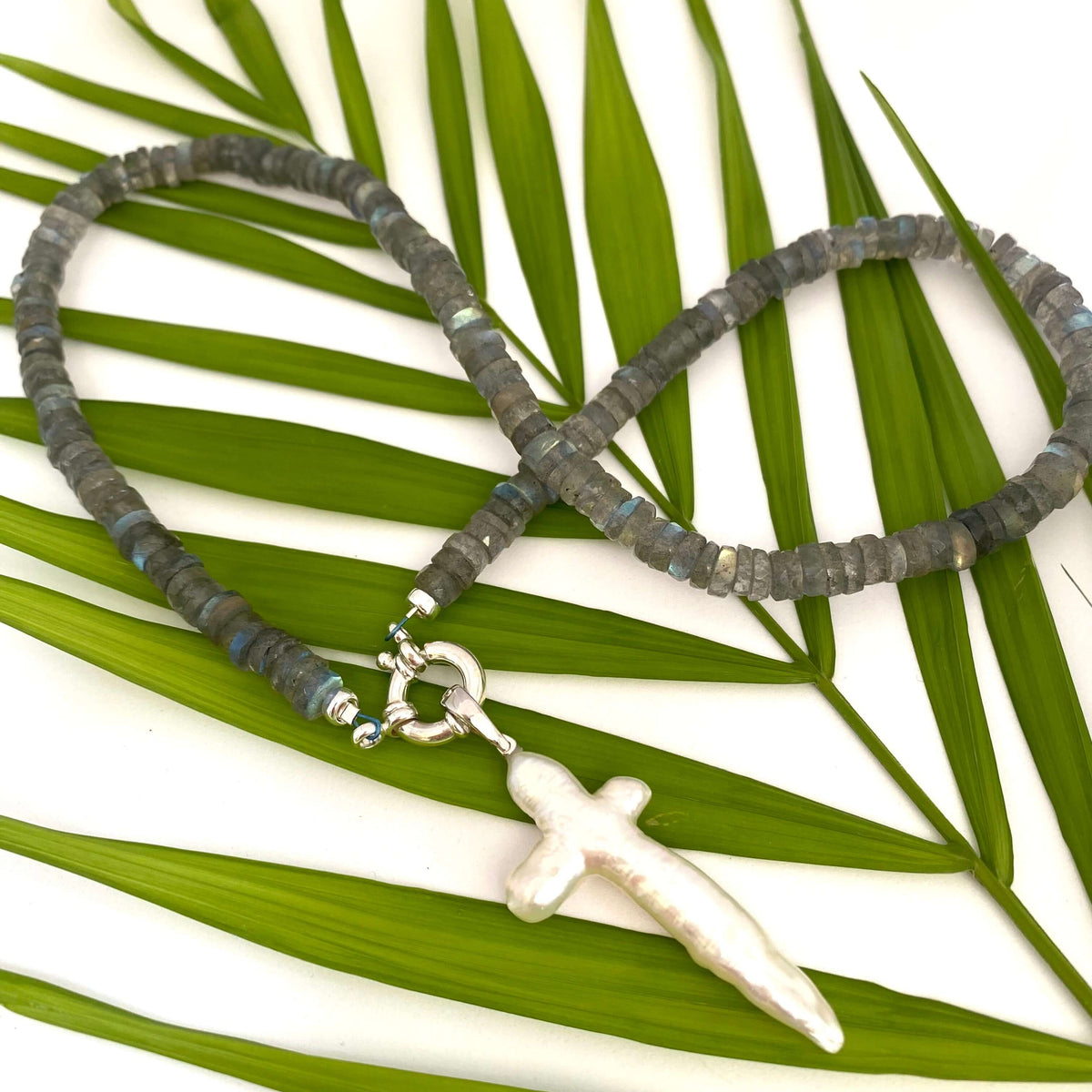 Handcrafted labradorite necklace with pearl cross photographed outdoors with green leaves — artisan jewelry by Loulia Pearl Jewelry