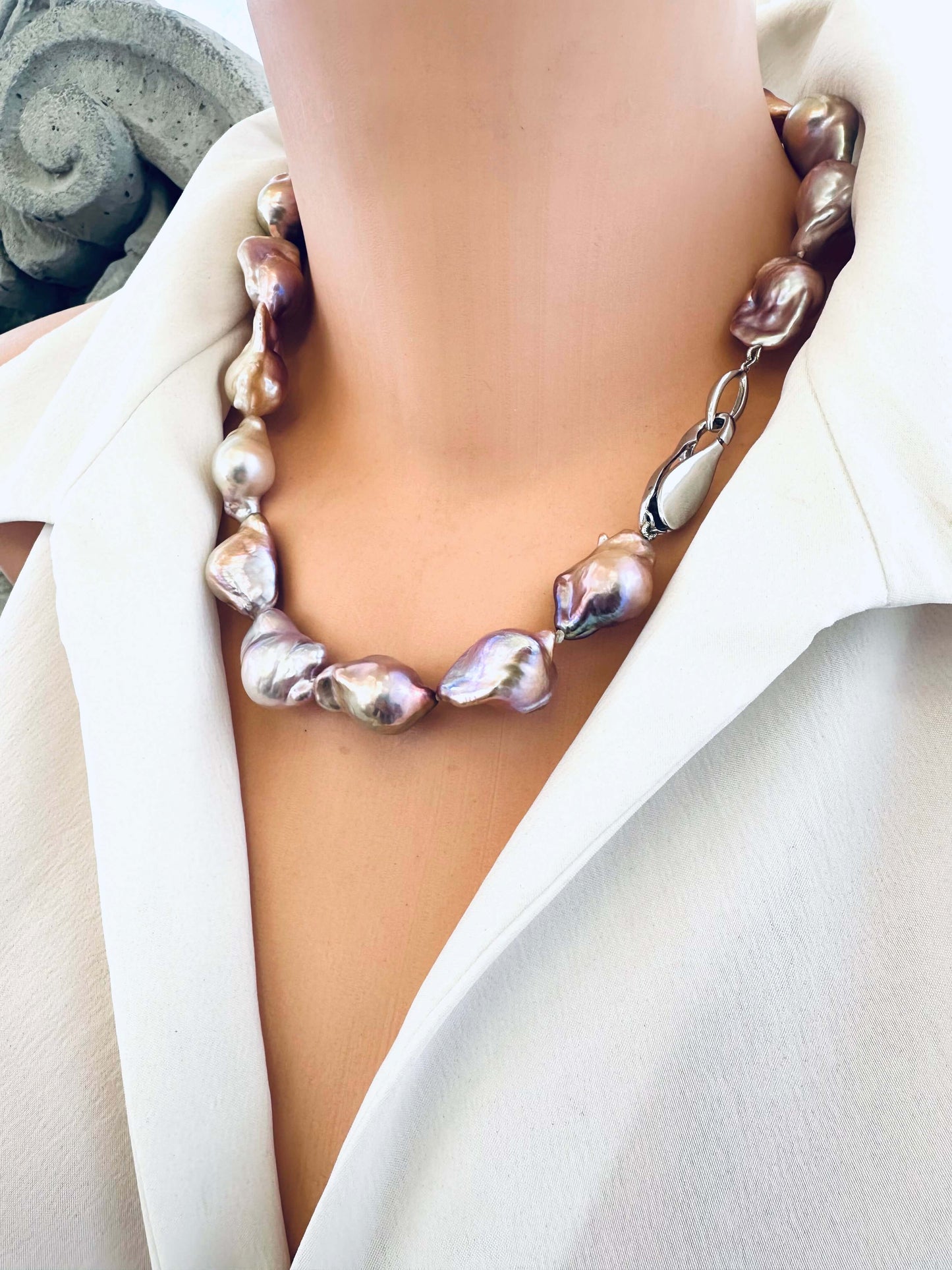 Pearl necklace worn by a person in a white outfit, with a neutral background