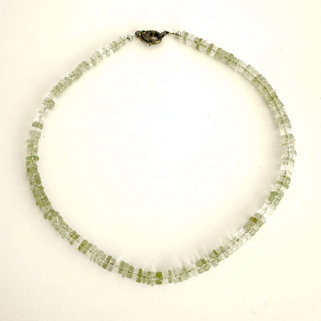 A beaded necklace made of small, faceted light green gemstone beads, arranged in two rows and secured with a dark metal clasp, shown on a plain white background.