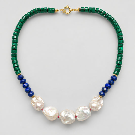 A beaded necklace featuring dark green faceted beads, a section of deep blue round beads, and five large white baroque pearls at the center, finished with a gold clasp, shown on a light gray background.