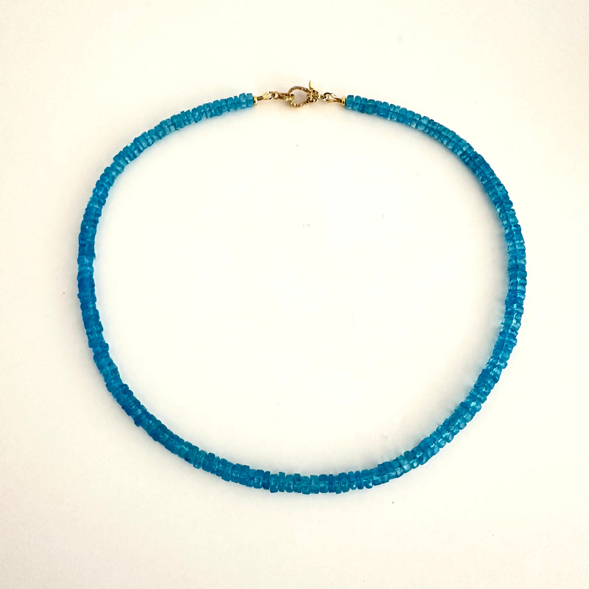 A beaded necklace made of small, faceted blue-green glass beads with a gold clasp, displayed on a plain white background.