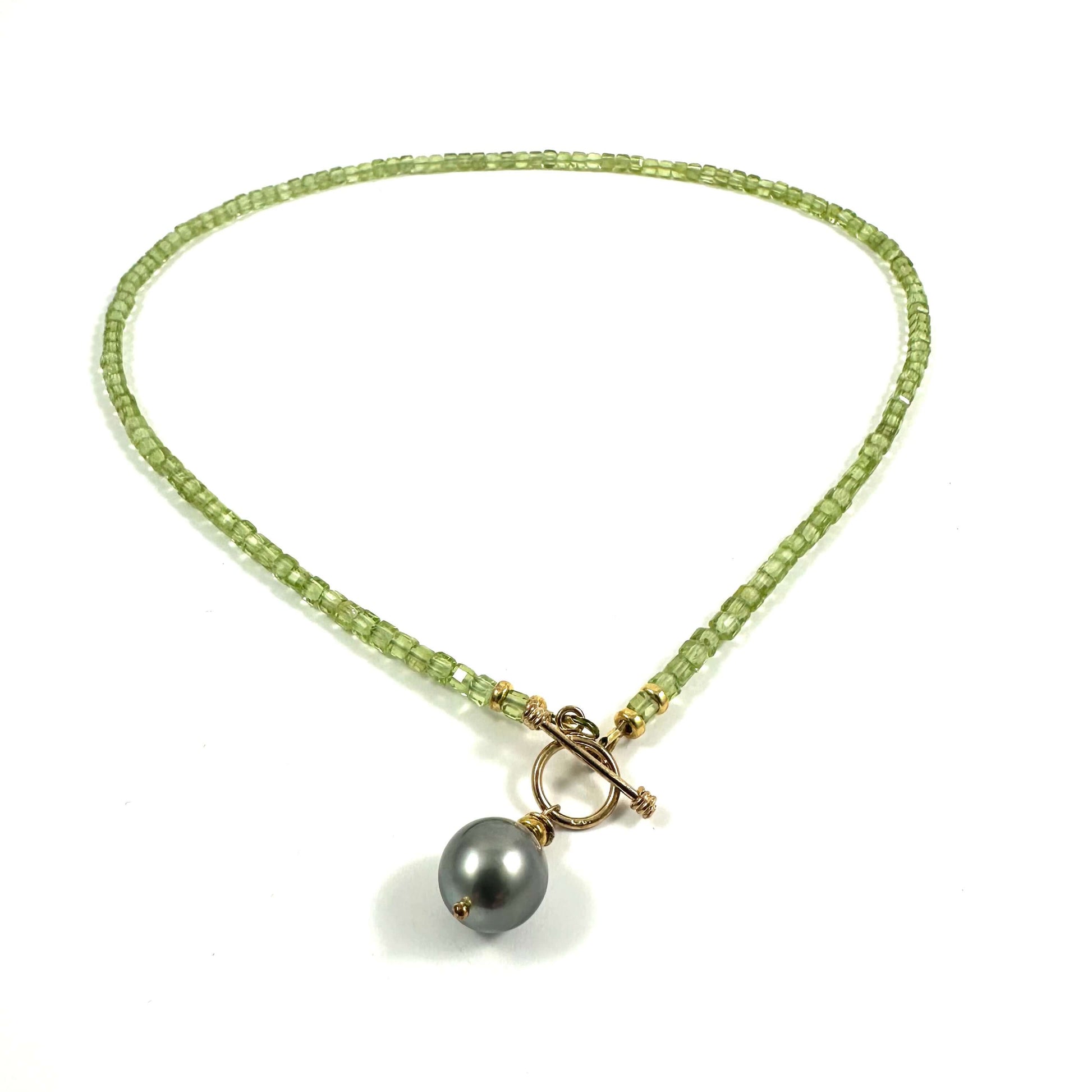 A beaded necklace featuring light green square beads, a gold-tone toggle clasp, and a single dark gray pearl pendant, displayed on a clean white background.