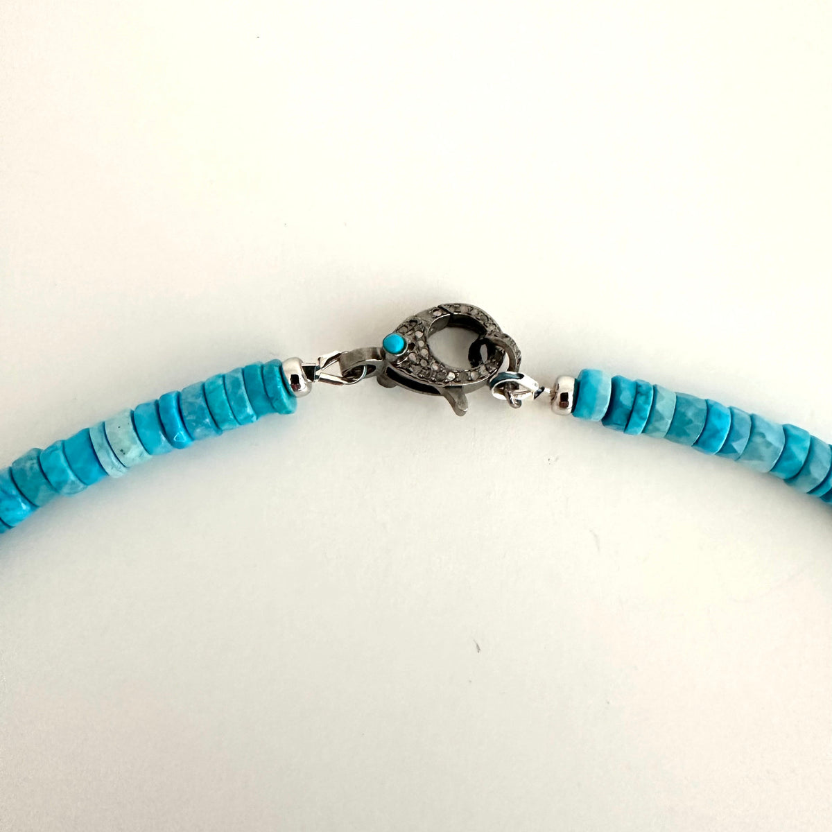 A close-up of a turquoise beaded necklace with a silver-toned textured clasp, shown against a plain white background.