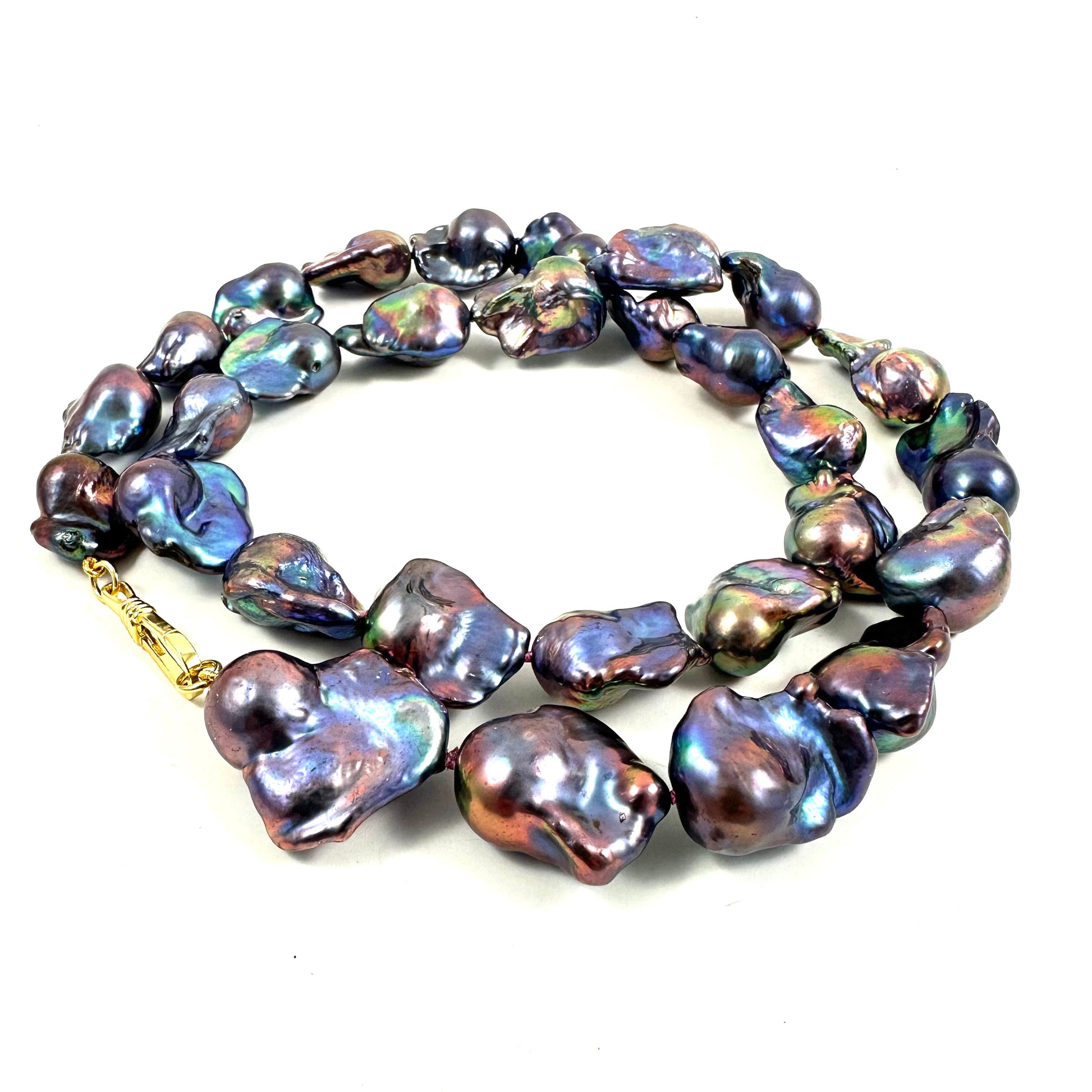 A strand of baroque freshwater pearls with an iridescent, multi-tonal sheen of purple, blue, green, and bronze, accented by a gold clasp, shown on a plain white background.