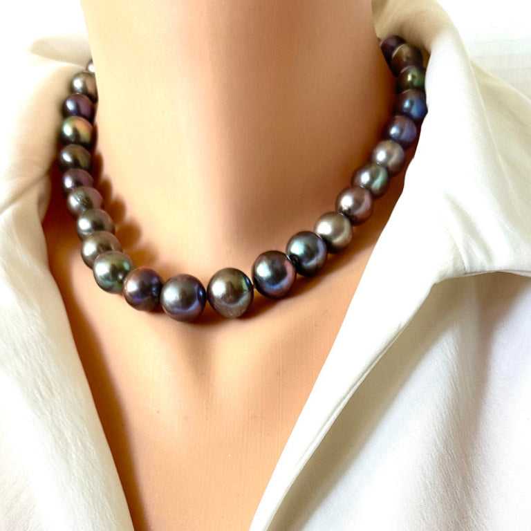 A strand necklace of dark, iridescent freshwater pearls styled on a mannequin torso wearing a white collared shirt.