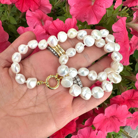 Small baroque pearl classic necklace displayed on a hand, surrounded by colorful pink flowers.