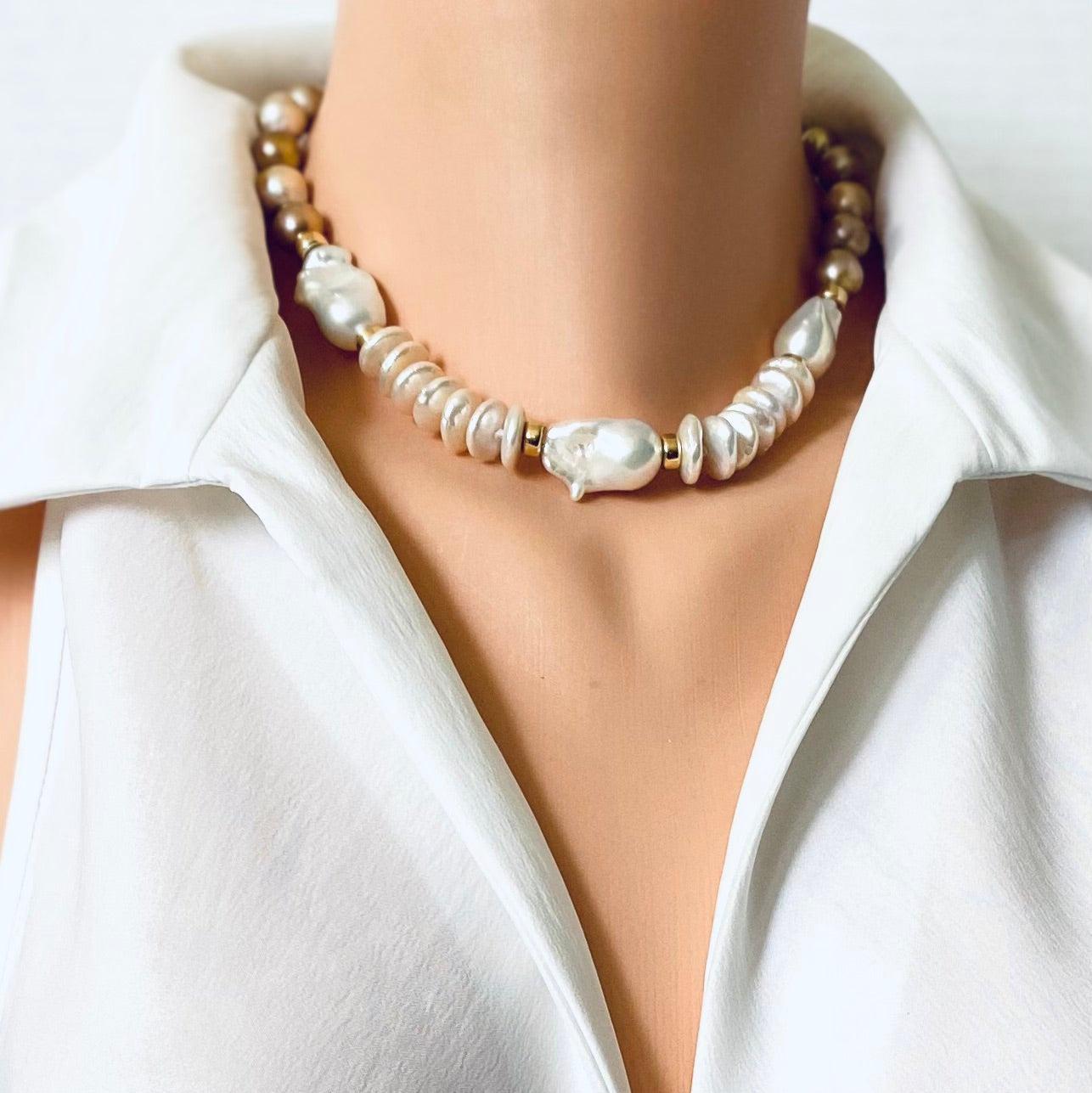 A close-up of a model wearing a pearl and gold beaded necklace with baroque pearls, styled with a white collared shirt.