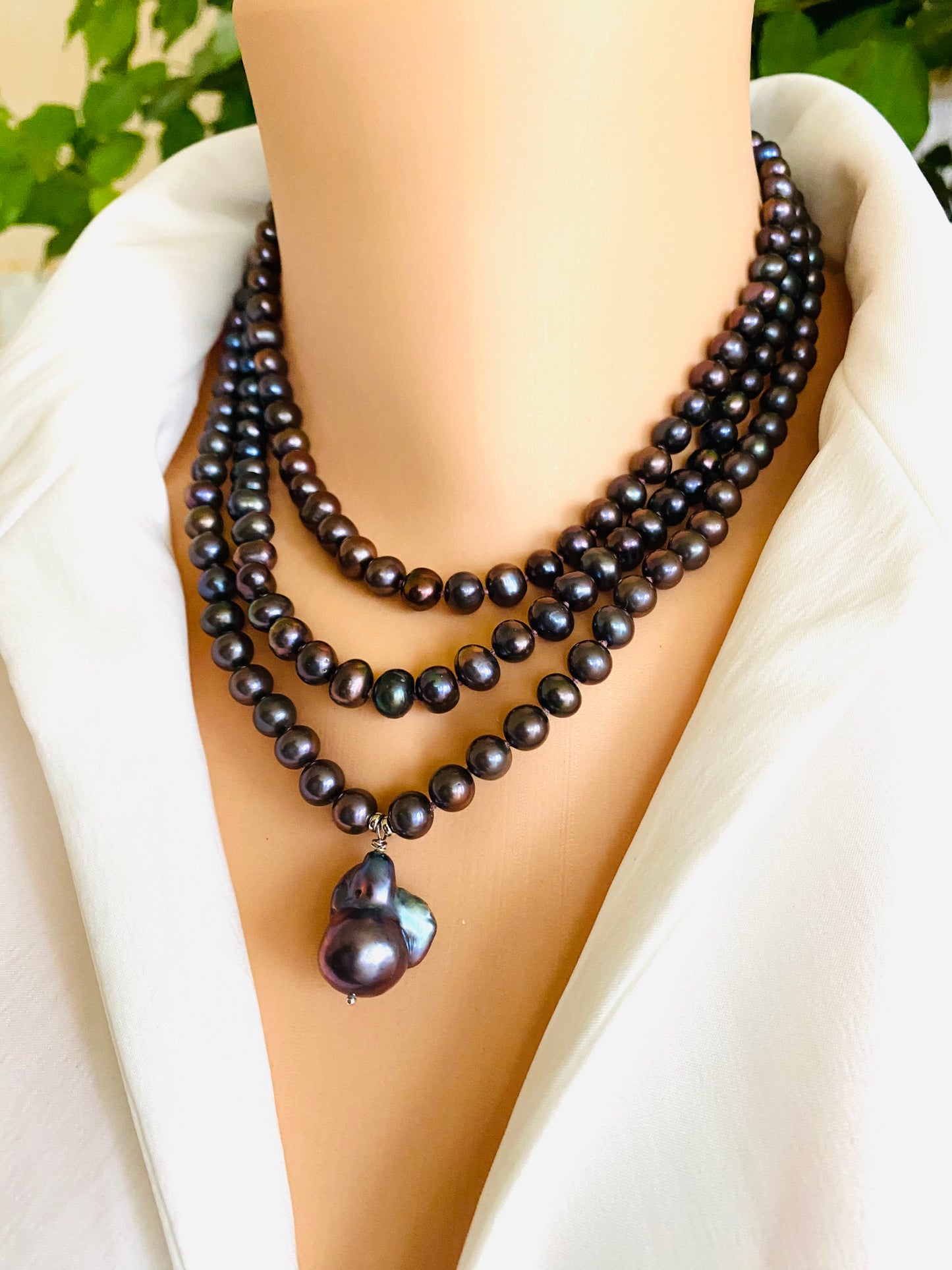 Black pearl necklace on a mannequin with a white garment and green leaves in the background