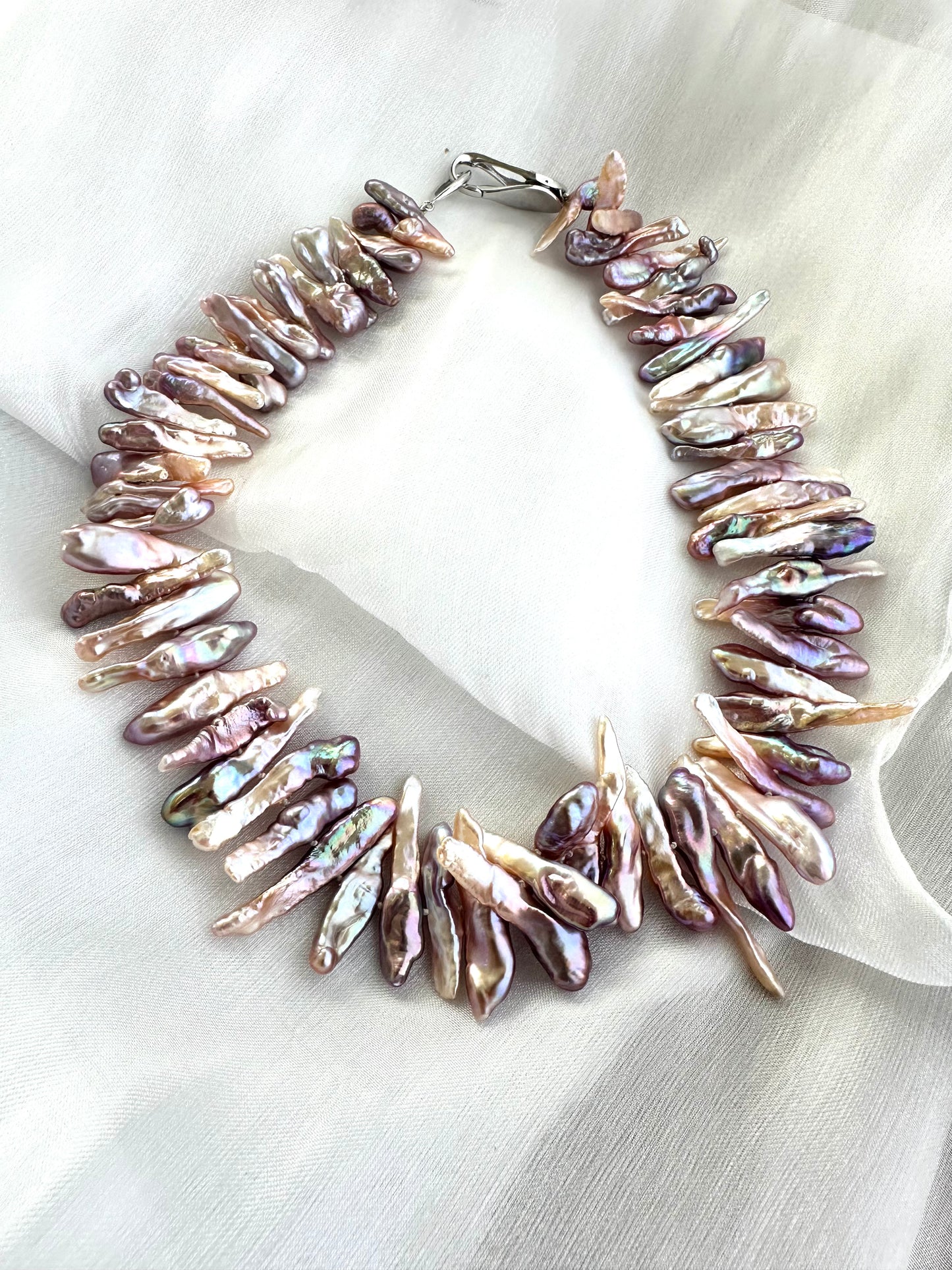 Biwa Pearl Necklace with purplish long stick pearls displayed on white fabric background.
