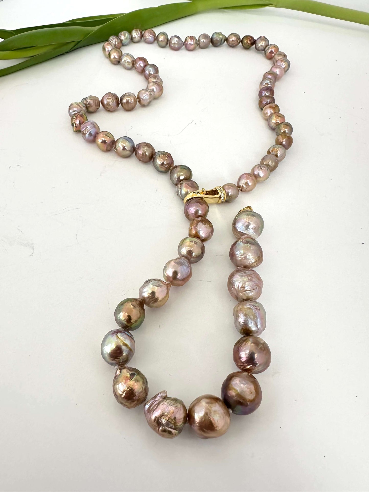 Pearl necklace on a white surface with green leaves in the background