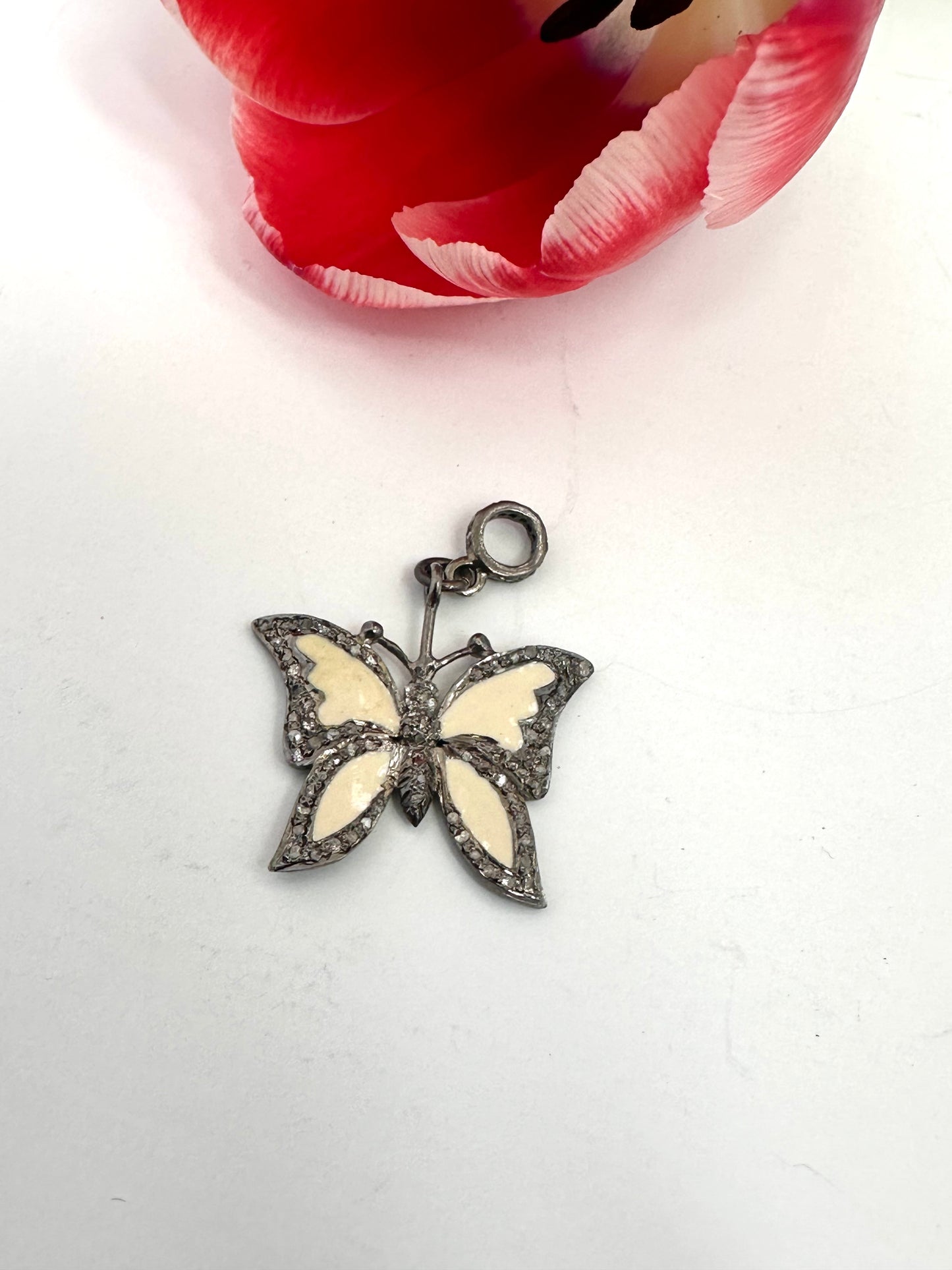 Butterfly-shaped pendant on a white background with a red flower in the corner.