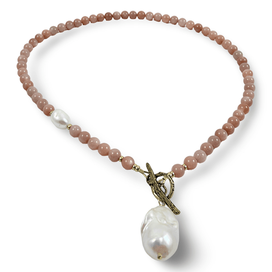 A beaded necklace featuring dusty rose quartz beads, a single white pearl spacer, and a large baroque pearl pendant suspended from an antique bronze toggle clasp, shown on a clean white background.