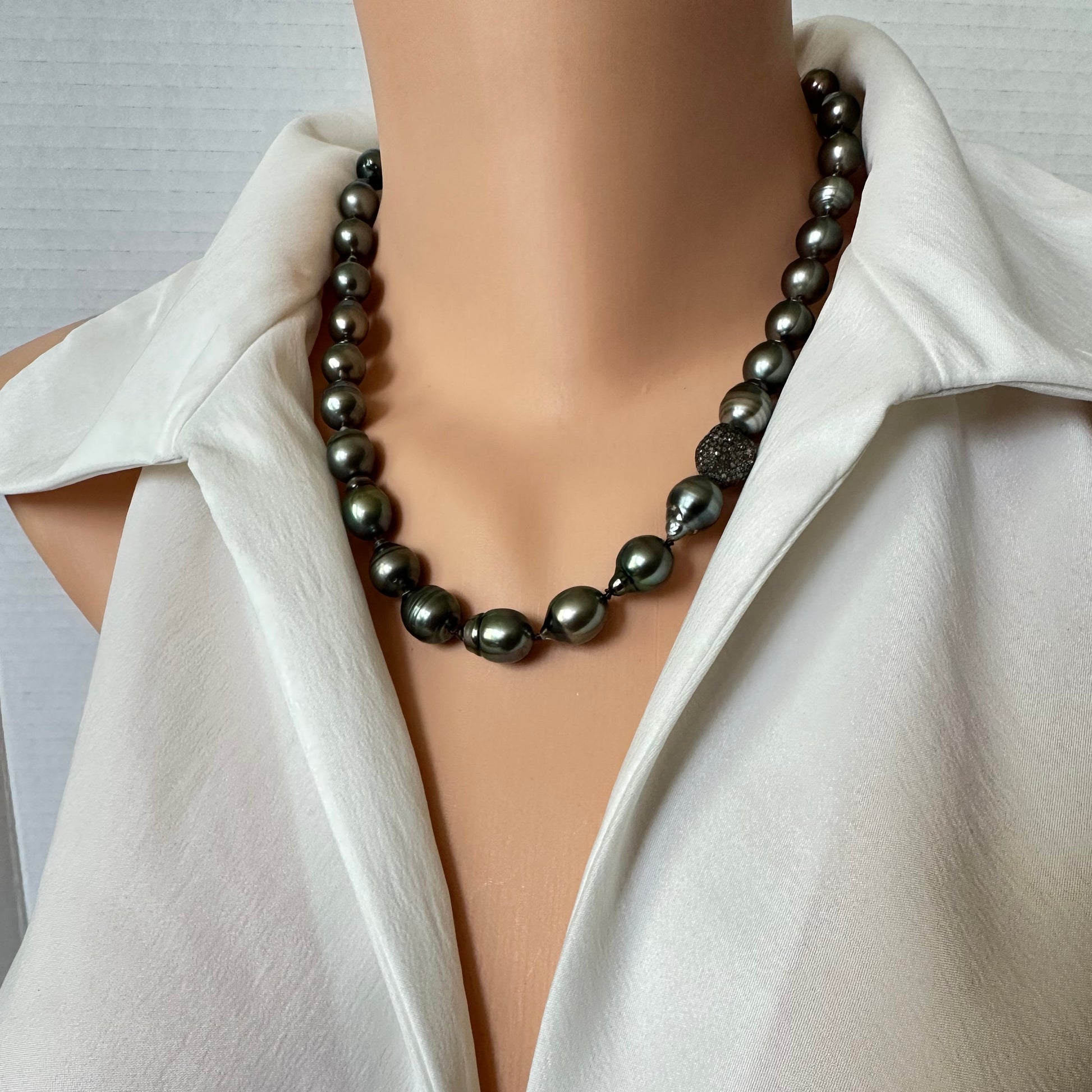 A dark charcoal gray baroque pearl necklace displayed on a mannequin torso wearing a white satin blouse.