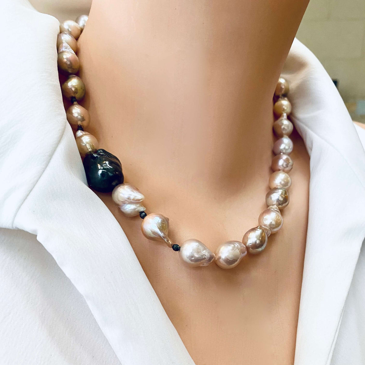 Side close-up of pink baroque pearl necklace worn by mannequin, black rhodium silver clasp visible.