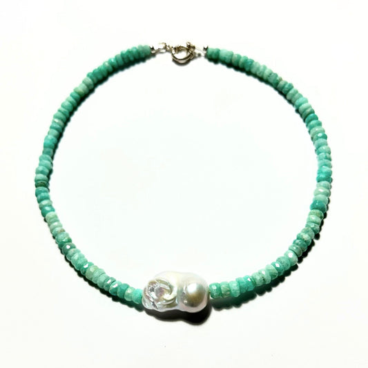 A beaded necklace featuring small, round amazonite-green beads with a central white baroque pearl embellished with a silver-toned skull and a clear crystal. The necklace is displayed on a clean white background.