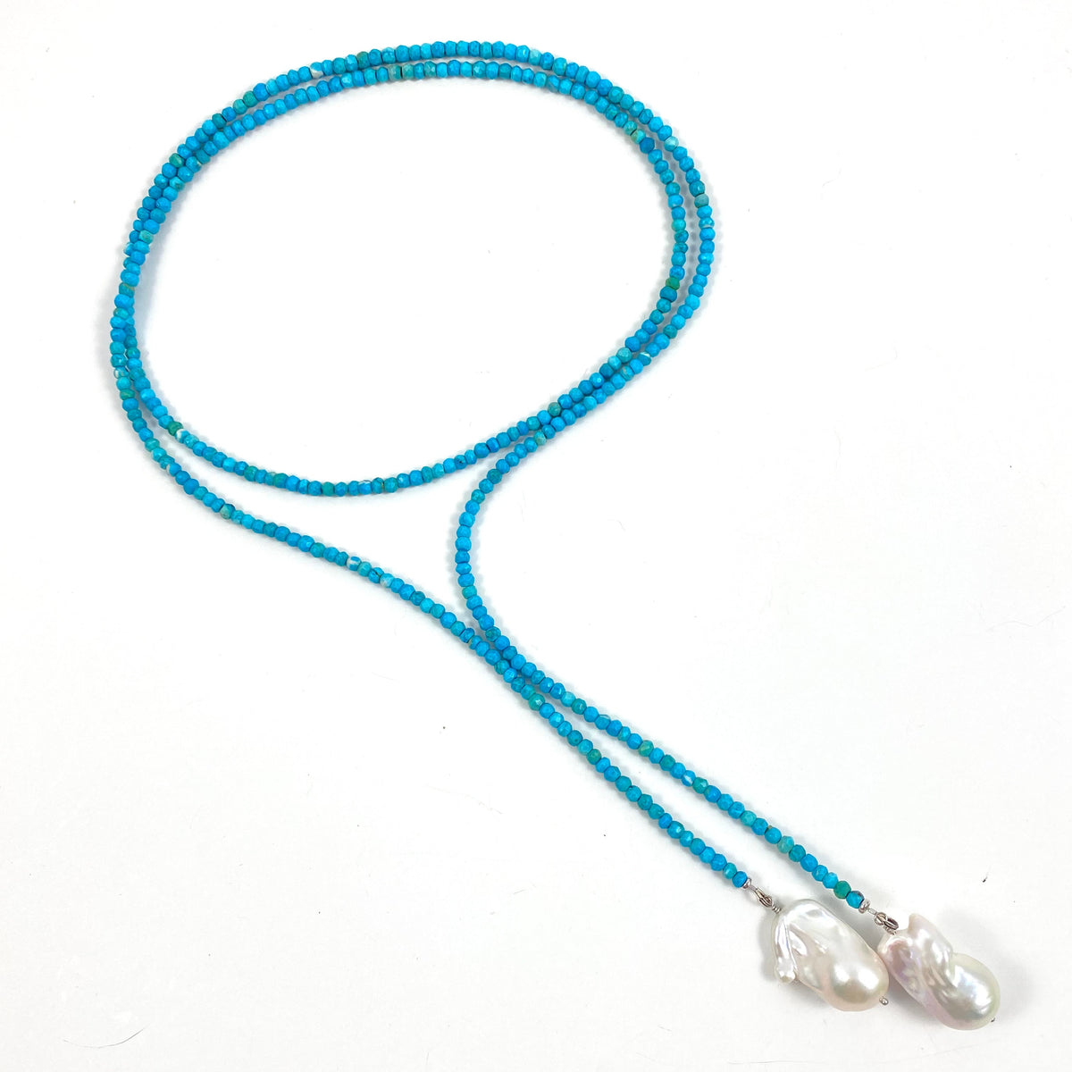 A turquoise blue beaded necklace with two white baroque pearls at the end, displayed on a clean white background.