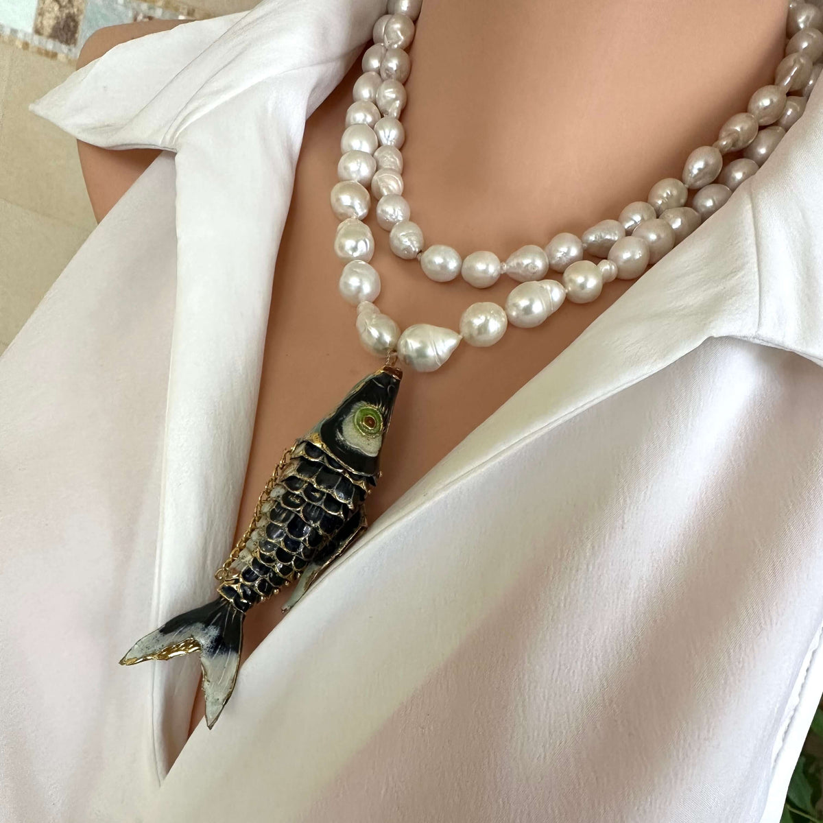 Fish pendant pearl necklace featuring a black cloisonné fish on a strand of baroque pearls.