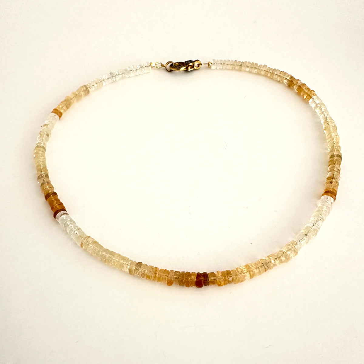 A beaded necklace made of small translucent and opaque beads in white, cream, and warm brown tones, arranged in a circle on a plain off-white background.