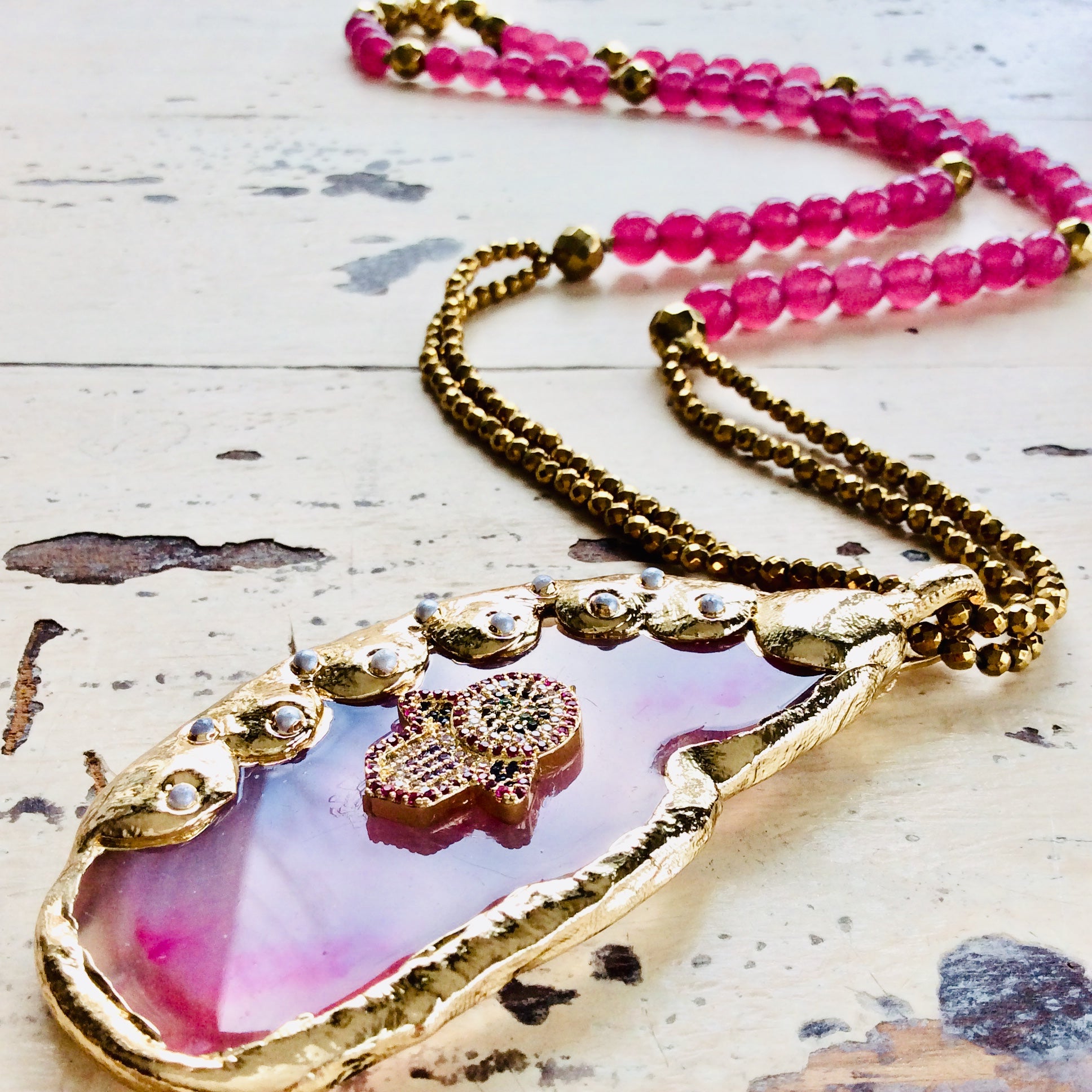 Hot pink agate pendant necklace featuring a gold-electroplated design and CZ Hamsa symbol on a beaded chain.