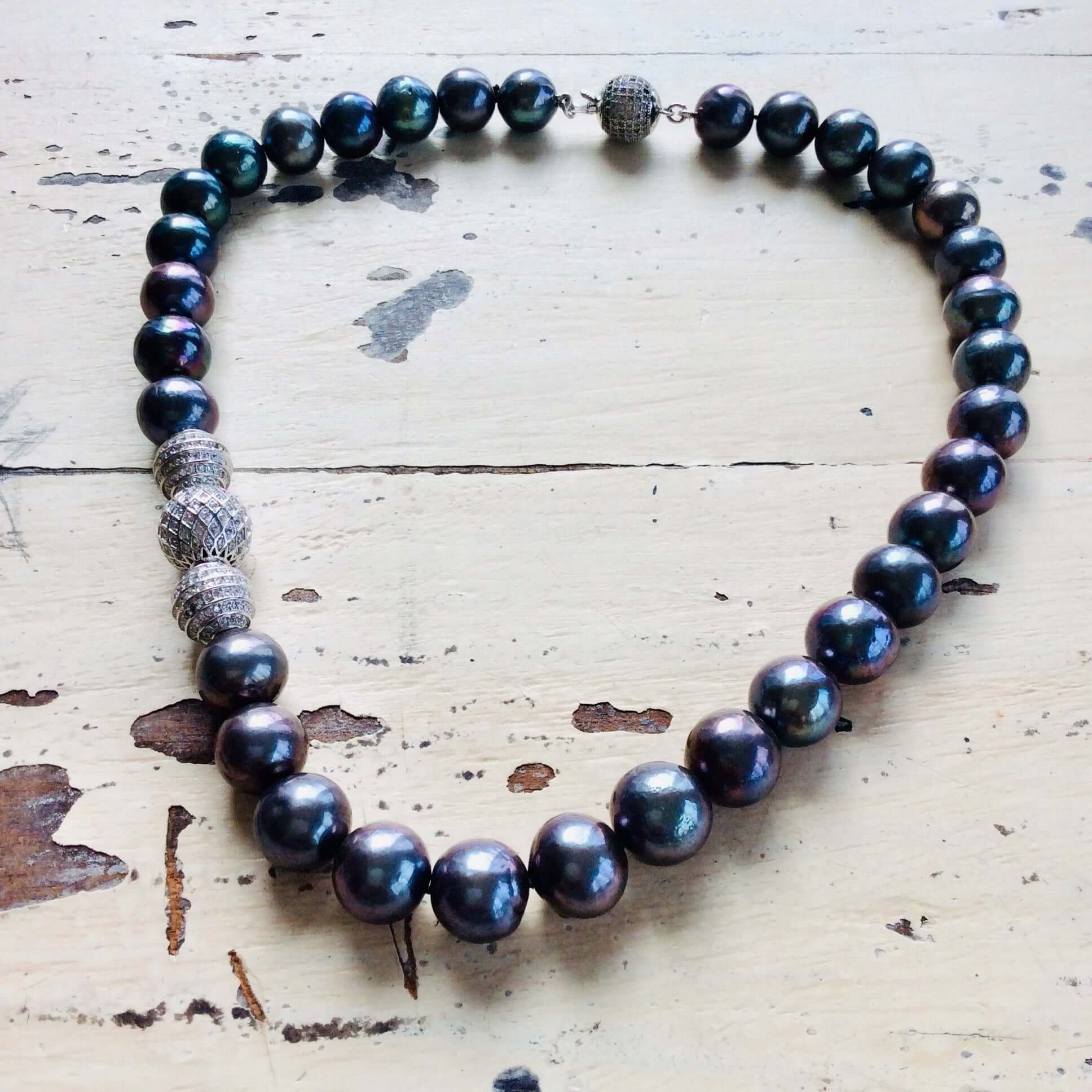 Close-up of freshwater black pearl silver necklace on white wood surface highlighting rhodium silver clasp