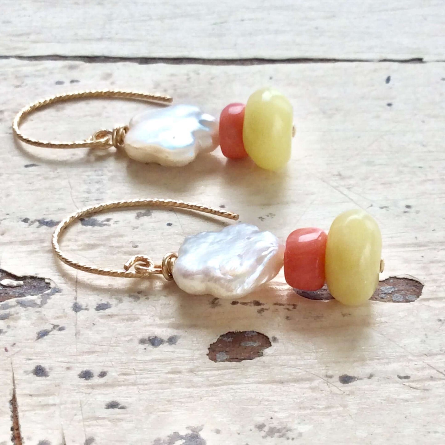 Dainty pearl drop earrings featuring baroque pearls, pink coral, and green quartz gemstones on a rustic wooden surface.