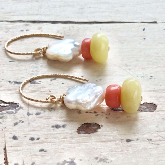 Dainty pearl drop earrings featuring baroque pearls, pink coral, and green quartz gemstones on a rustic wooden surface.