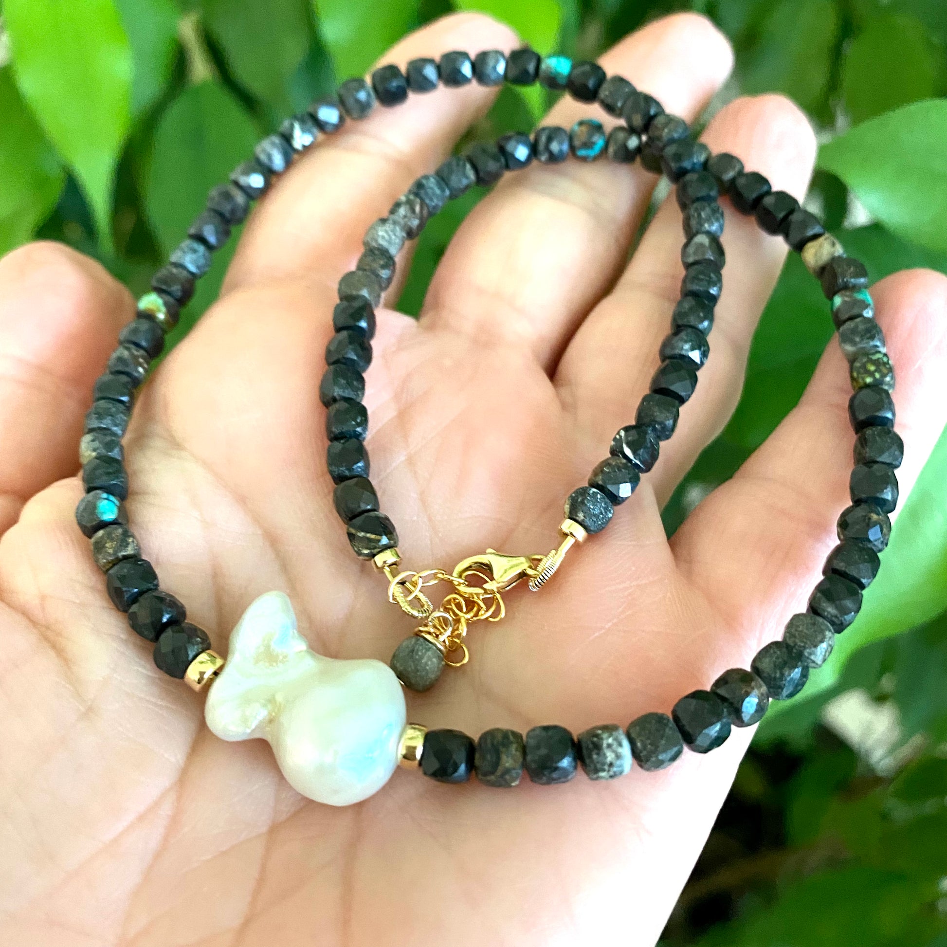 Black turquoise baroque pearl necklace with faceted cube beads and gold filled details held in hand