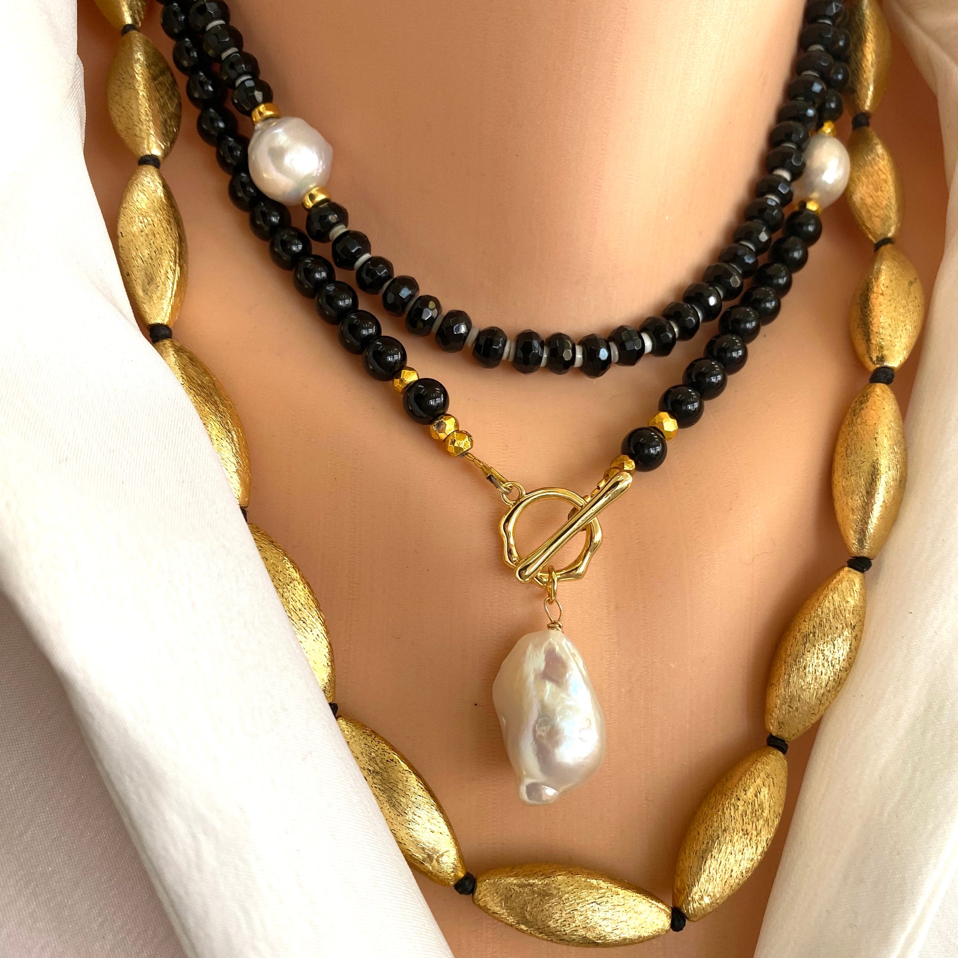 Black onyx pearl choker necklace layered with gold chain featuring white baroque pearl detail