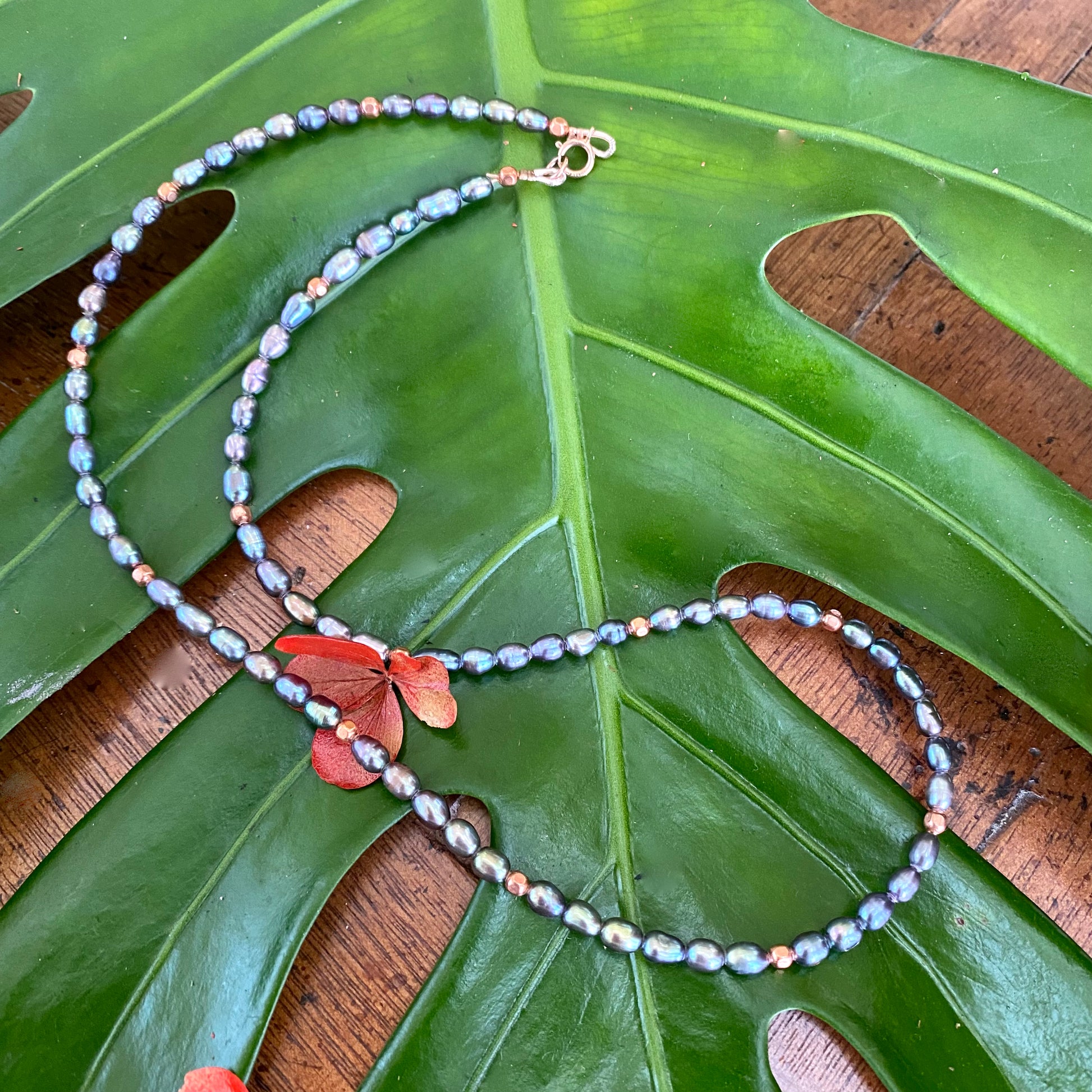 Black pearl necklace gold filled flat lay on leaves, peacock pearls with solid copper bead details