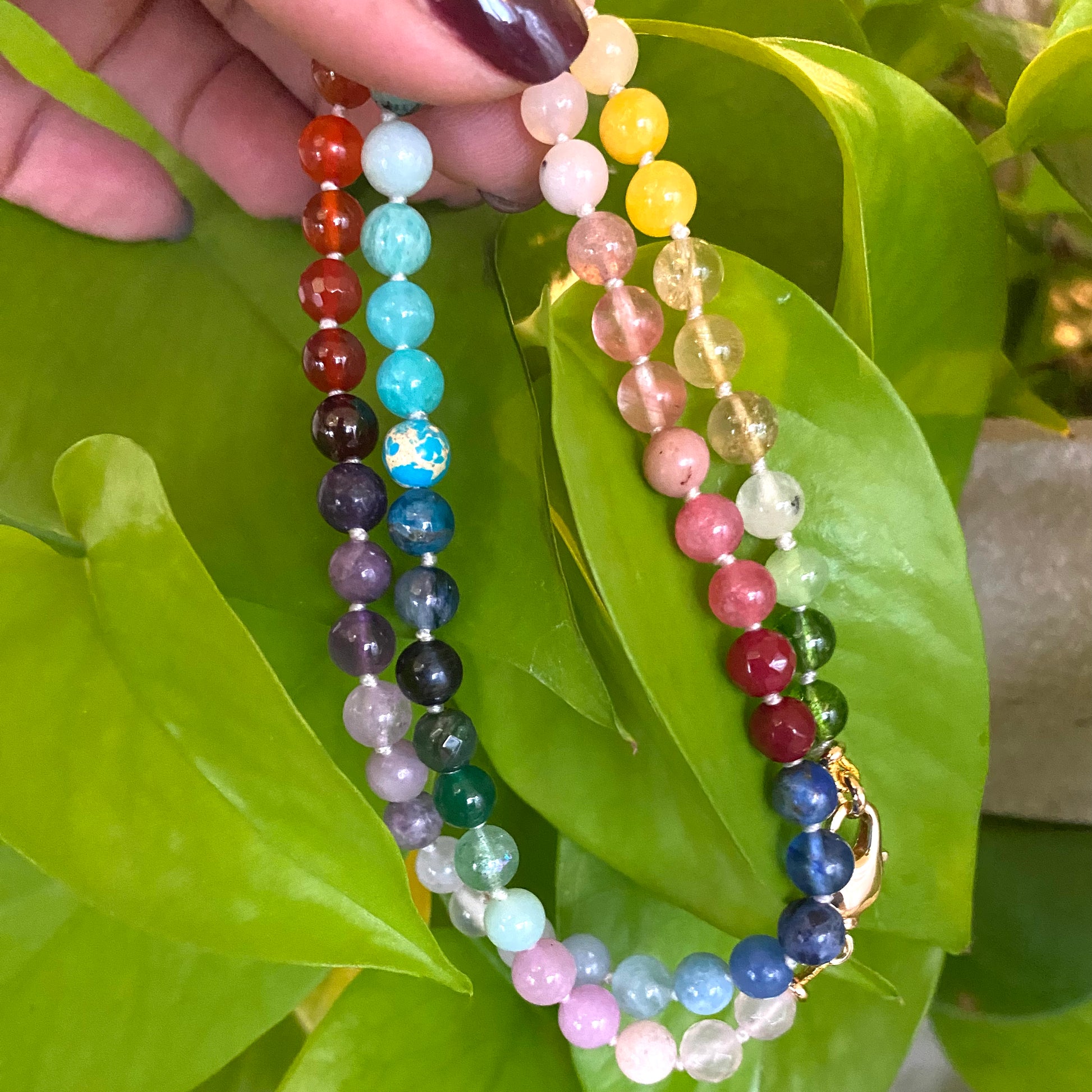 Rainbow candy necklace in mini gemstone beads displayed against green leaves.