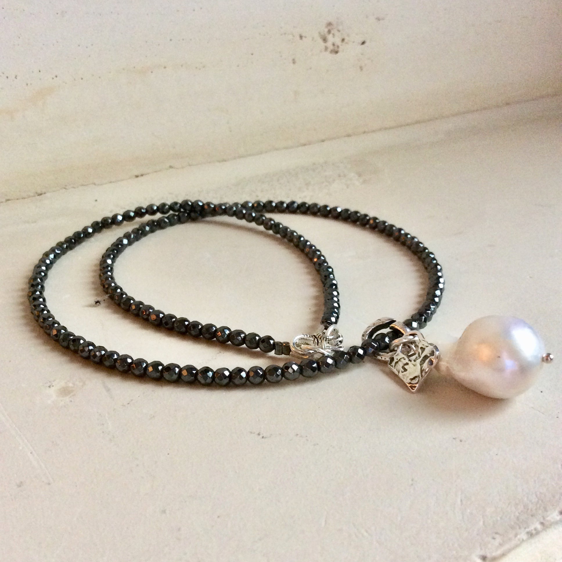 Hematite necklace with baroque pearl pendant displayed flat showing faceted hematite beads