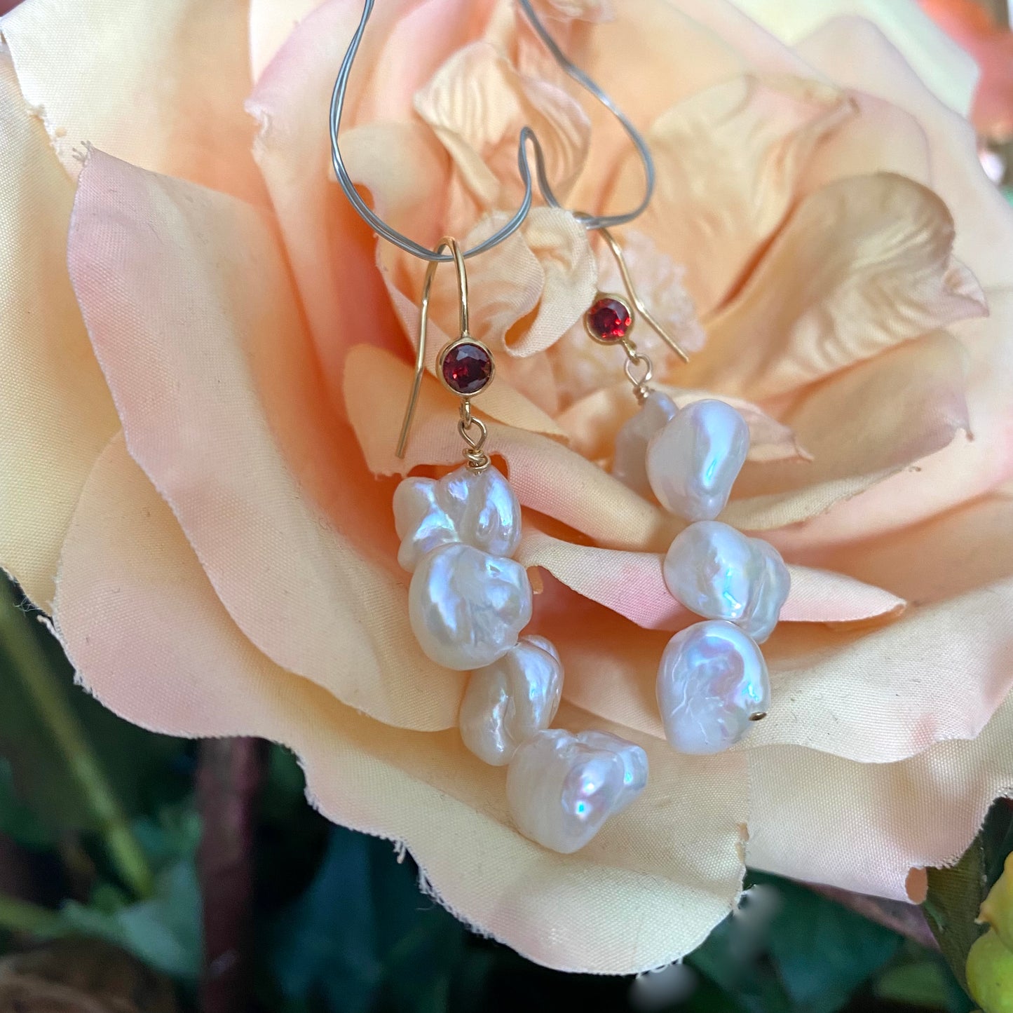 Pearl drop earrings with keshi pearls and red CZ, showcasing unique elegance against a soft rose background.