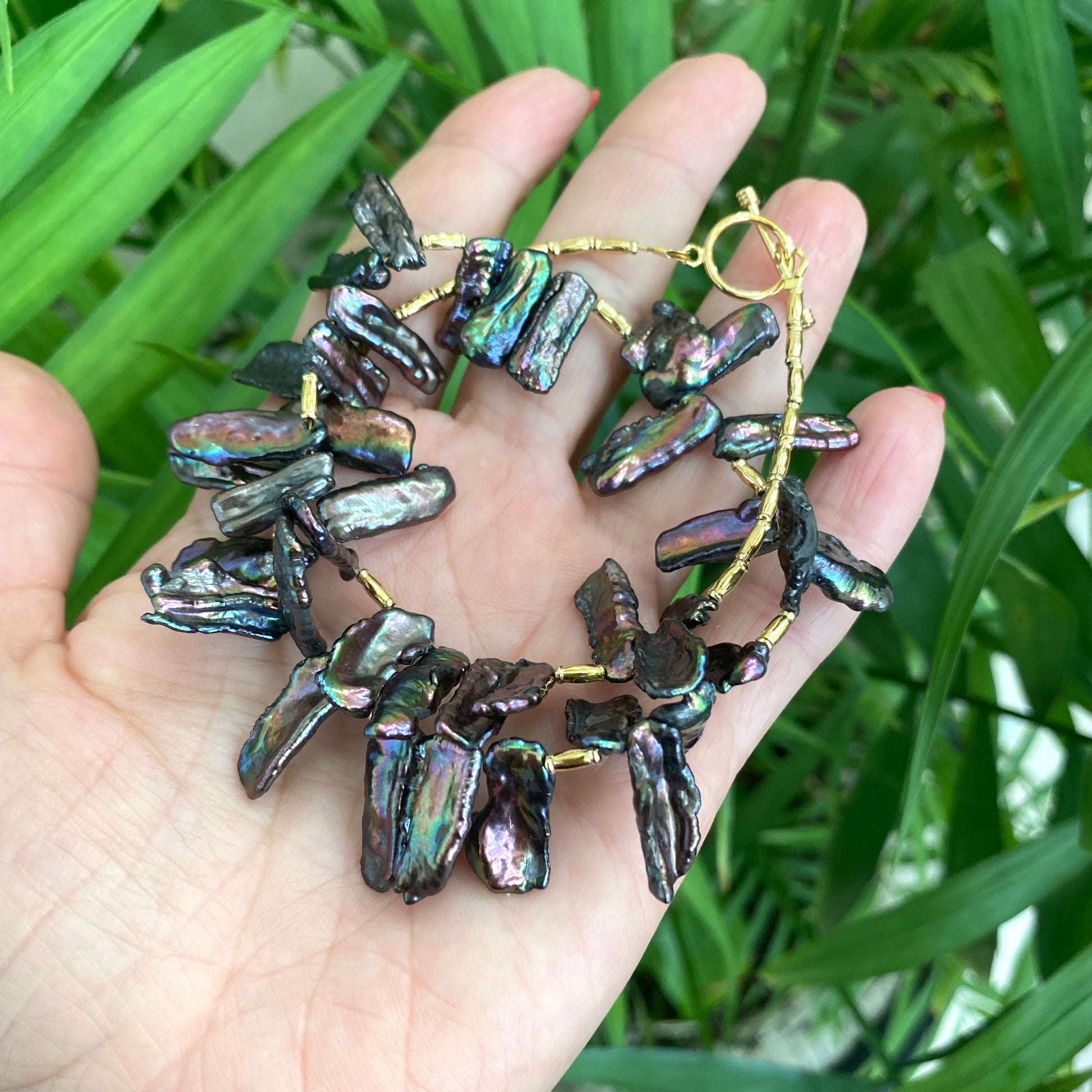 Black pearl choker necklace in hand, peacock Biwa stick pearls showing purple green teal shine