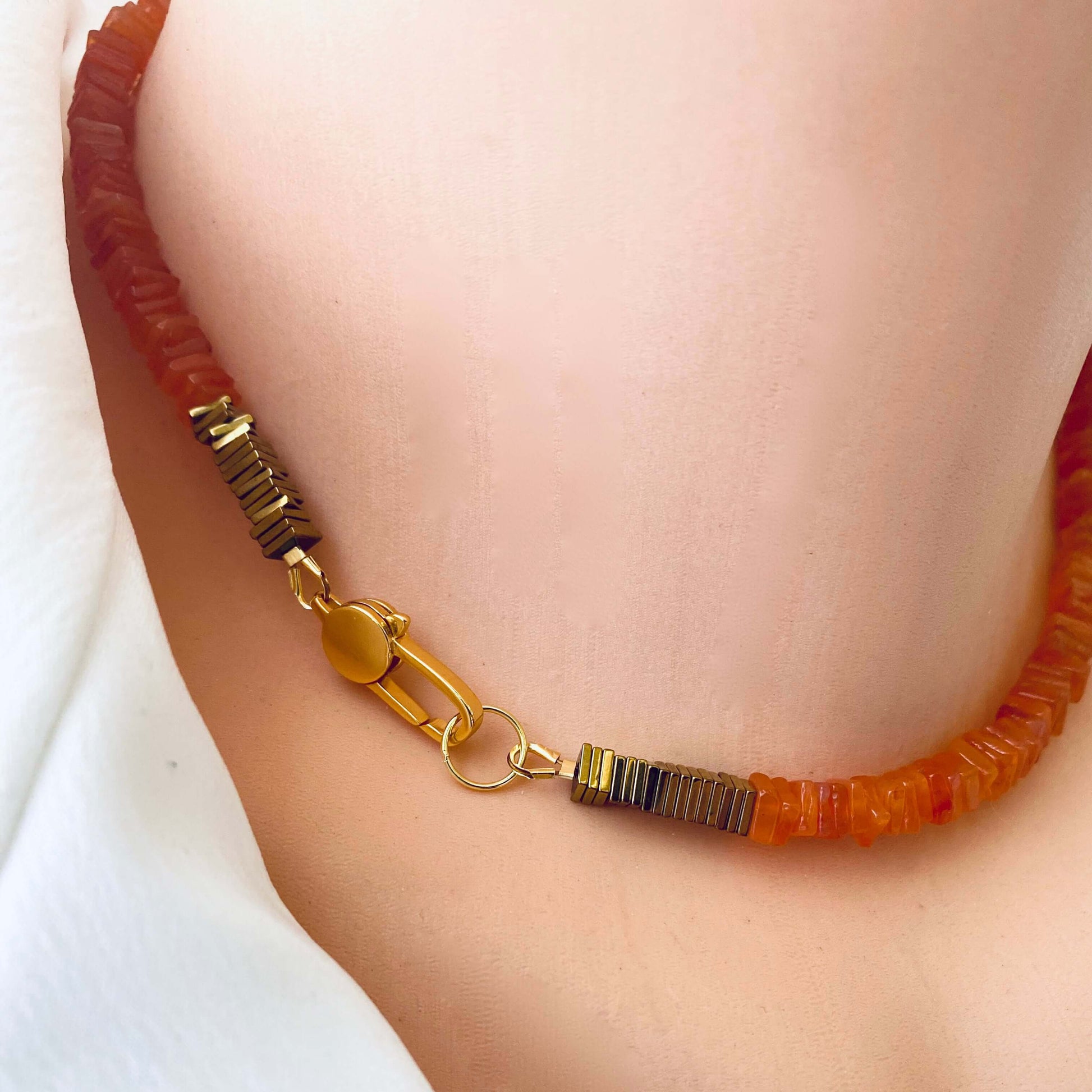 Close-up of a carnelian choker necklace featuring bright orange gemstone beads and gold clasp, showcasing its vibrant design.