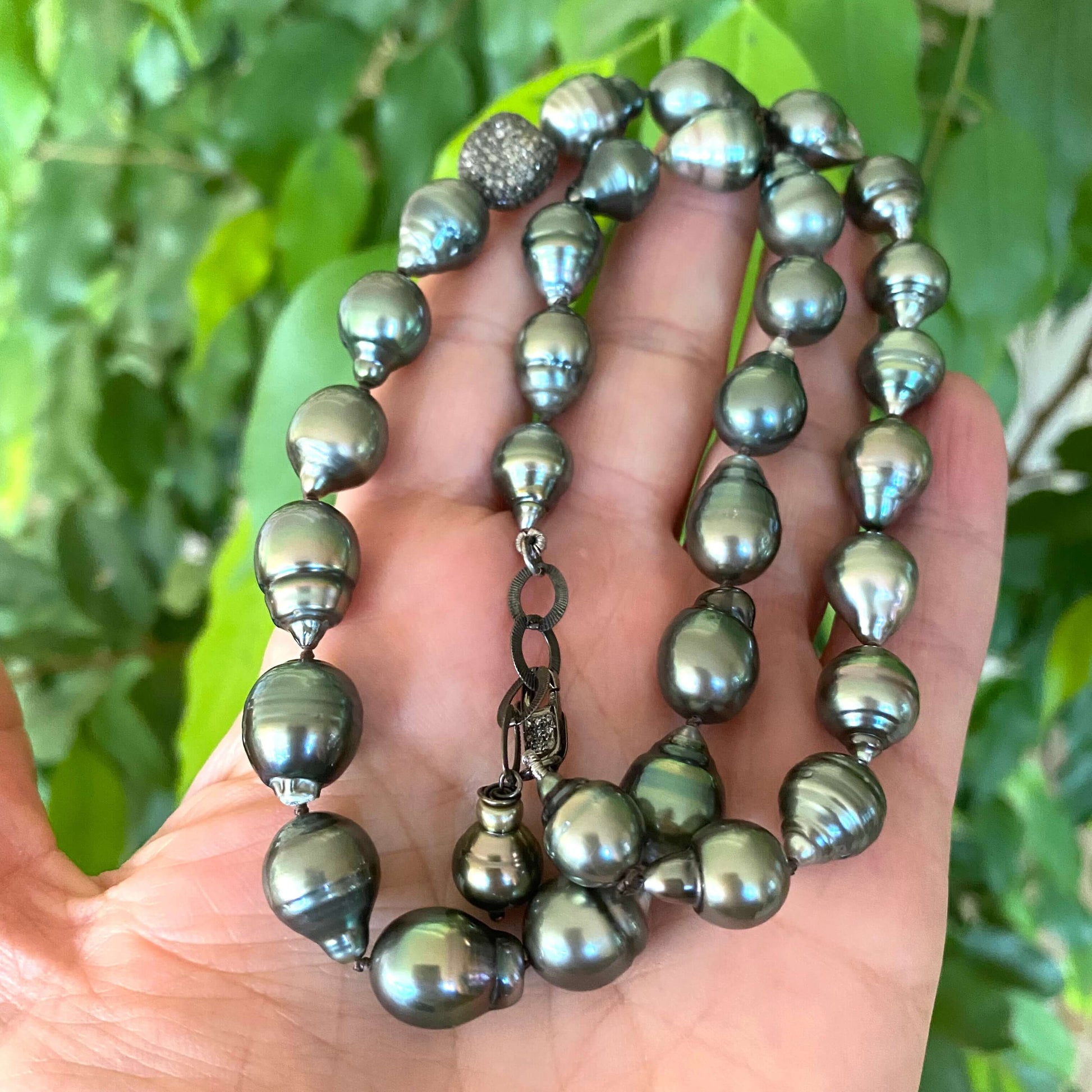 Tahitian baroque pearl necklace with champagne diamonds elegantly displayed in a hand against a green background.