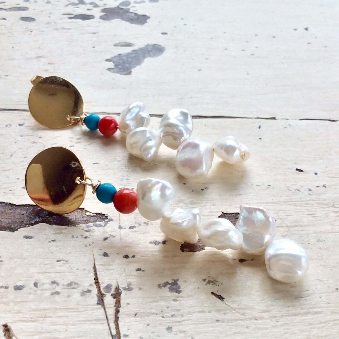 Baroque Keshi Pearl Earrings with gold dangle and turquoise, red coral accents on a rustic background.