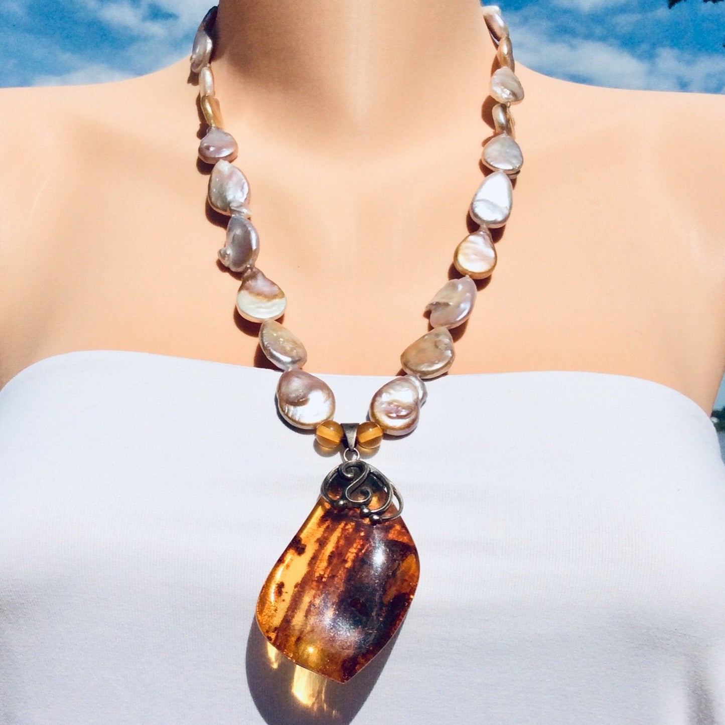 Frontal close-up of keshi pearl necklace worn by mannequin, organic pearls and amber pendant.