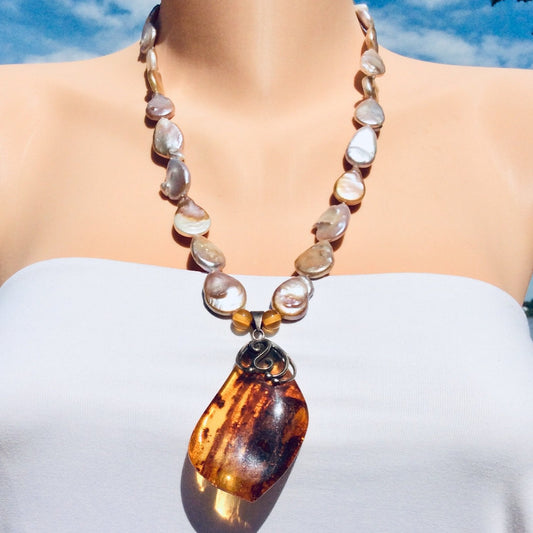 Frontal close-up of keshi pearl necklace worn by mannequin, organic pearls and amber pendant.